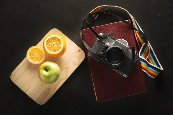 Фото старой камеры крупным планом на старых книгах с фруктами на черном фоне — стоковое фото