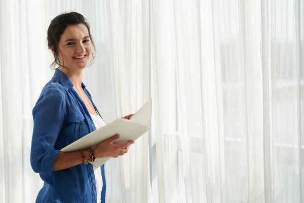 Woman standing at window with documents — Stock Photo, Image