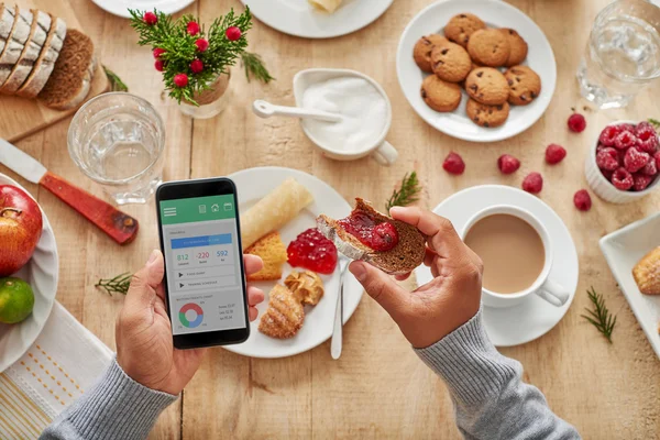 Mand spiser morgenmad med smartphone i hånden - Stock-foto