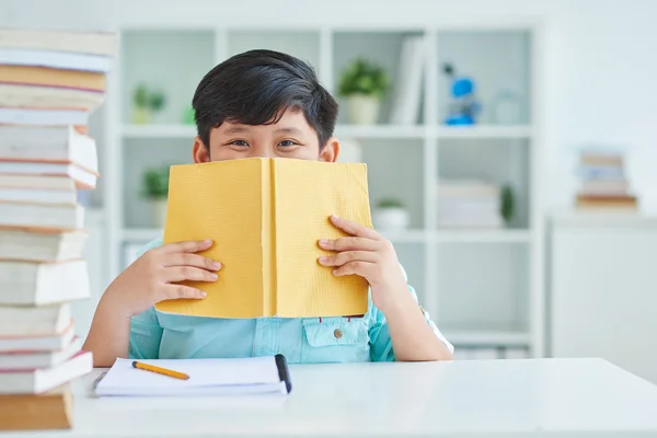 Skolpojke gömmer sig hans leende bakom boken — Stockfoto