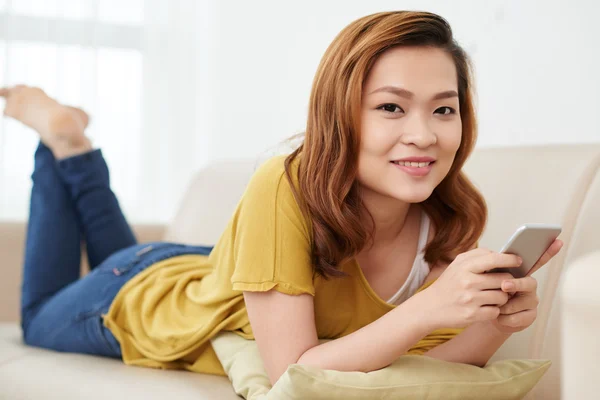 Жінка лежить на дивані зі смартфоном — стокове фото