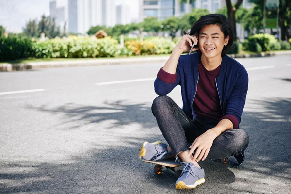 Uomo che chatta sul telefono seduto skateboard — Foto Stock