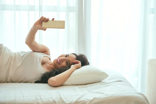 Женщина делает селфи в постели — стоковое фото