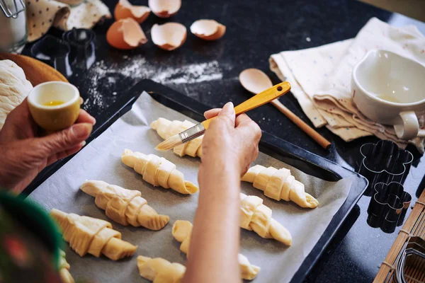 Mulher que cobre croissants com gema de ovo — Fotografia de Stock