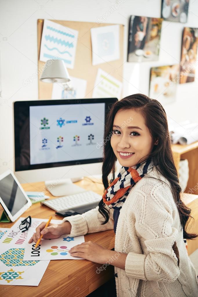 Asian graphic designer working on new project in office while looking at camera
