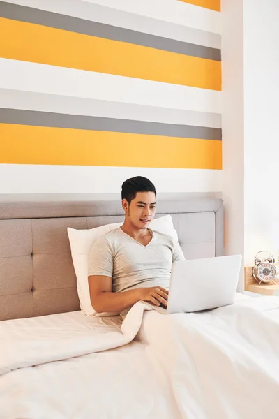 Man sitting in bed with laptop on knees — Stock Photo, Image