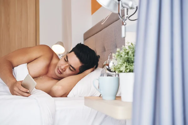Mężczyzna w łóżku, za pomocą aplikacji w telefonie — Zdjęcie stockowe