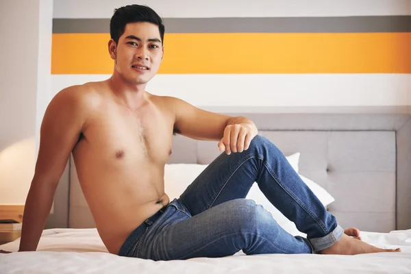 Человек в джинсах, сидящий на кровати — стоковое фото