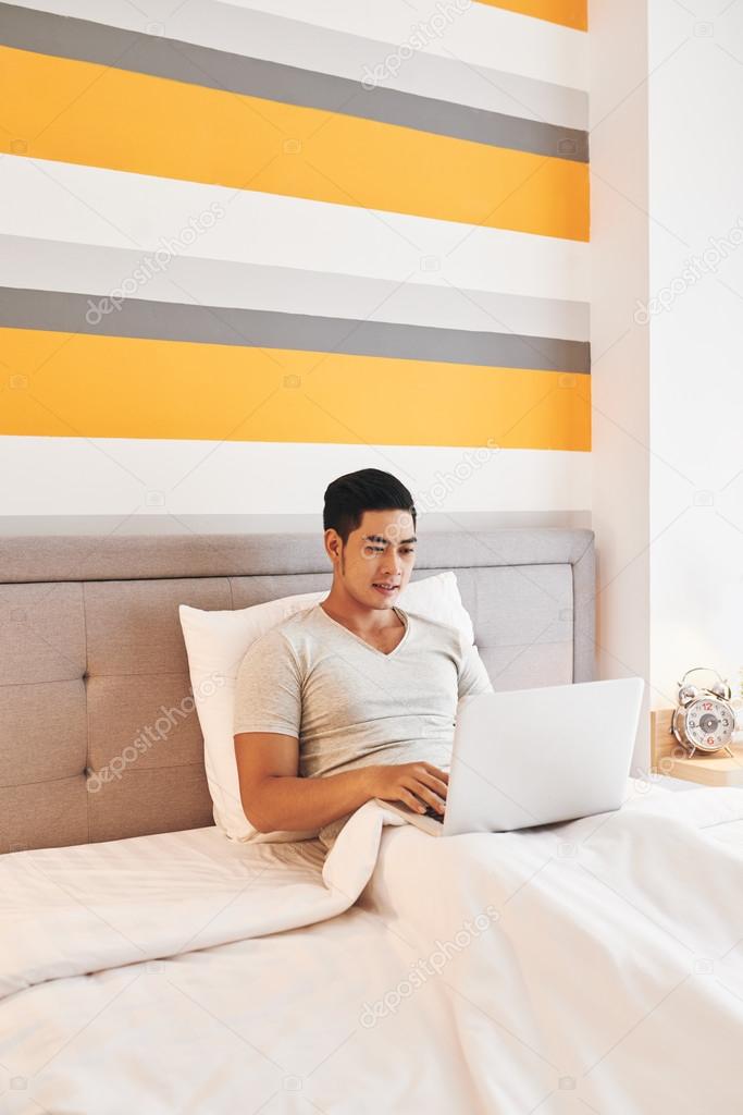 man sitting in bed with laptop on knees