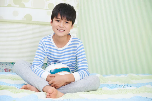 Boy with soccer ball sitting on bed — Stock Photo, Image