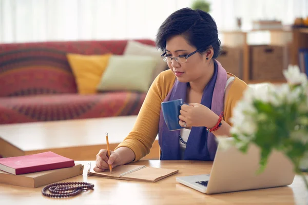 Frau trinkt Kaffee und schreibt in Notizblock — Stockfoto