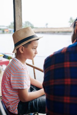 Babası ona nasıl balık tutulacağını açıklarken ciddi ciddi göle bakan küçük bir çocuk.