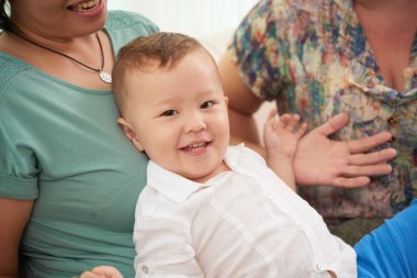 Neşeli melez çocuk annesinin kucağında dinleniyor ve kameraya gülümsüyor.