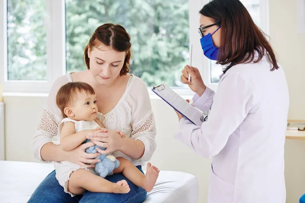 Pediatra Máscara Médica Conversando Com Menina Tomando Notas Cartão Médico — Fotografia de Stock