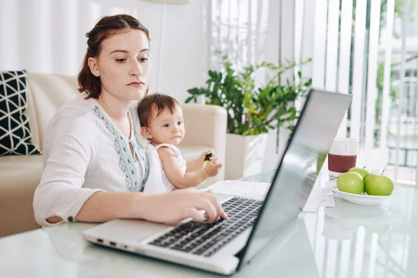 Mujer Joven Seria Sentada Mesa Con Bebé Sus Vueltas Trabajando — Foto de Stock