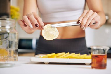 Soğuk çay için kavanoza limon koyan genç bir kadının elleri. 