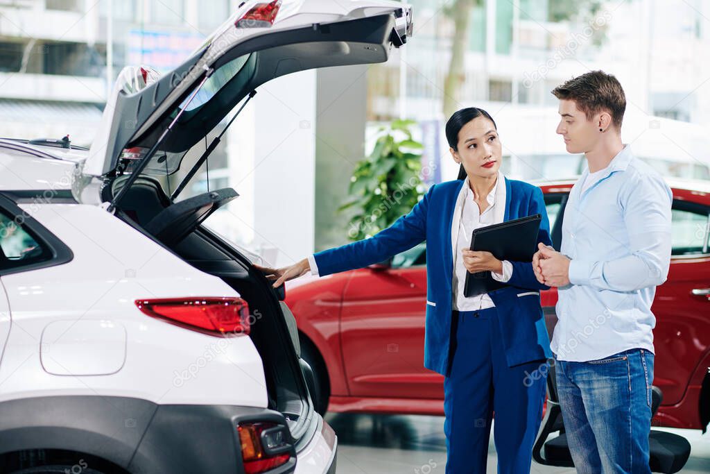 Car dealership manager opening car trunk when showing automobile to customer