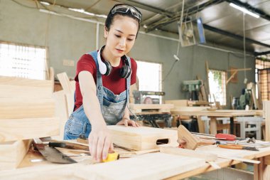 Güzel Vietnamlı genç marangoz atölyede yaptığı sandığı ölçmek için mezura alıyor.