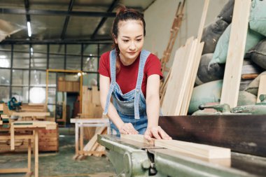 Gülümseyen Asyalı kadın marangoz tahta kesiyor.