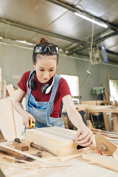 彼女はワークショップで顧客のために作る木製のクレートを測定若いアジアの大工 — ストック写真