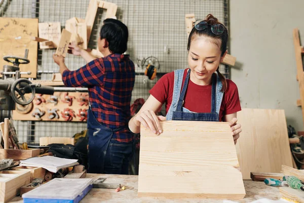 お客様のための家具アイテムを作る際に木製の板を選択するかなり女性大工の笑顔 — ストック写真