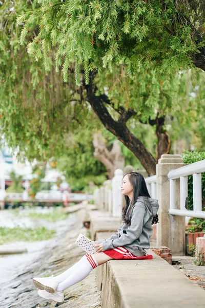 Pensive Koreaanse Schoolmeisje Met Boek Handen Zitten Oever Van Rivier — Stockfoto