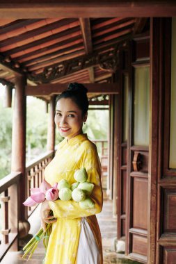 Geleneksel Aadai elbisesi içinde elinde bir buket nilüfer çiçeği tutan güzel, mutlu Vietnamlı kadın.