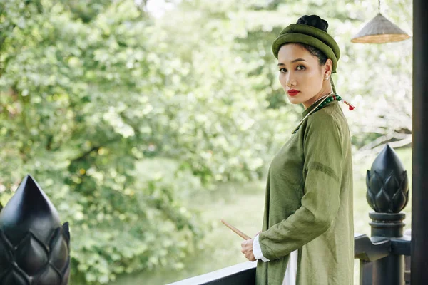 穿着传统绿色衣服的严肃的亚洲女人站在旧大楼阳台上看着相机的画像 — 图库照片