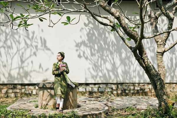 小戴的年轻貌美的女人穿着衣服 坐在花园里 捧着一束荷花 望着远方 — 图库照片