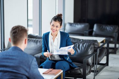 Neşeli genç iş kadını toplantıda iş arkadaşlarıyla raporları, çizelgeleri ve şemaları tartışıyor.
