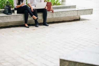 Açık havada oturup dizüstü bilgisayar üzerinde çalışan ve gelecek projeleri planlayan iş adamlarının kırpılmış görüntüsü.