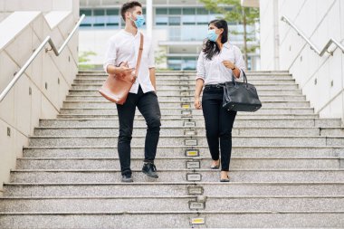 Koruyucu maskeli çok ırklı üniversite öğrencileri merdivenlerden inip sınıfları tartışıyorlar.