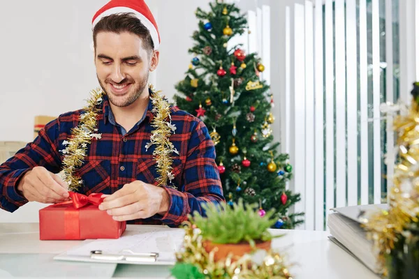 Podekscytowany Przystojny Biznesmen Rozpakowywanie Prezentu Świątecznego Gdy Siedzi Przy Stole — Zdjęcie stockowe