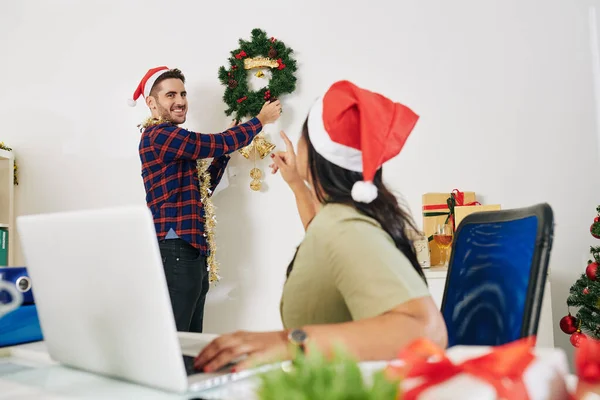 Επιχειρηματίας Στο Καπέλο Σάντα Ζητώντας Από Συνάδελφο Κρεμάσει Στεφάνι Χριστουγέννων — Φωτογραφία Αρχείου
