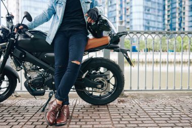 Bisikletçisine yaslanan yırtık kot pantolonlu kendine güvenen bir adamın kırpılmış görüntüsü.