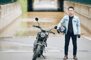 Kaskı elinde motorsikletinin yanında duran kendine güvenen yakışıklı Vietnamlı adam.