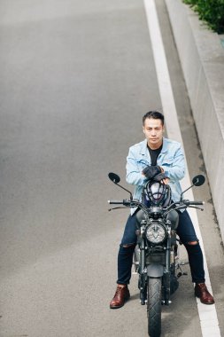 Ciddi derecede kendinden emin Vietnamlı bir adam motosiklette oturmuş kameraya bakıyor.