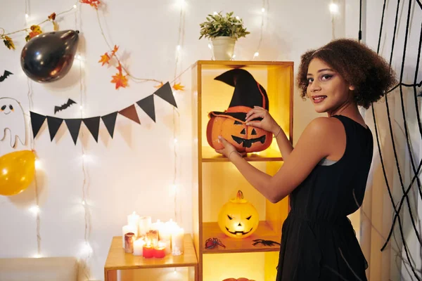 Mosolygó Tinédzser Lány Töklámpást Tesz Polcra Szobájában Halloweenkor Díszítve Kamerába — Stock Fotó