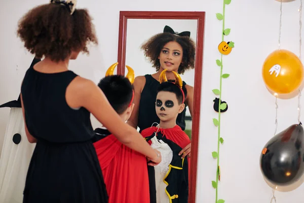 少年の前で海賊の衣装を身に着けている10代の女の子は鏡で自分自身を見て ハロウィーンの衣装を選択 — ストック写真