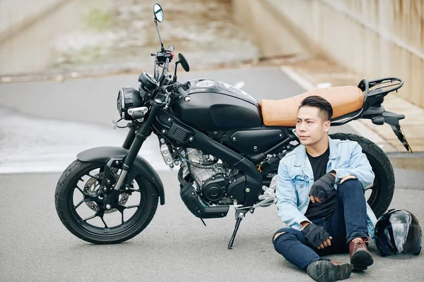 Ernsthaft Selbstbewusster Junger Asiate Sitzt Neben Motorrad Auf Dem Boden — Stockfoto