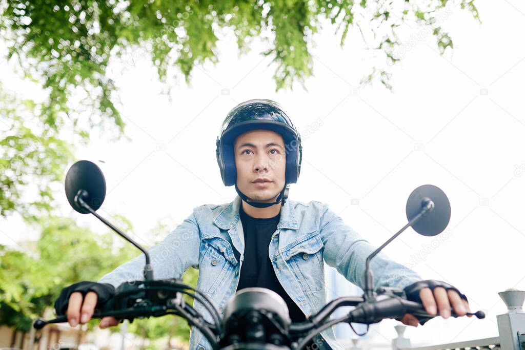 Young Vietnamese motorcyclist concentrated on road when riding fast in the city