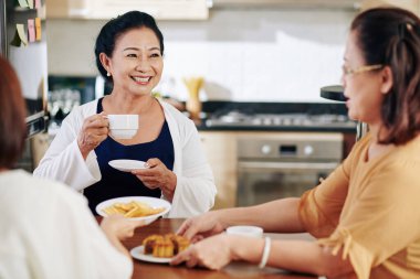 Arkadaşlarıyla sohbet ederken çay içip kurabiye yiyen son sınıf öğrencisi mutlu bir kadın.