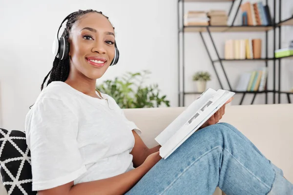 Preto Jovem Sorrindo Mulher Fones Ouvido Sentado Sofá Leitura Livro — Fotografia de Stock