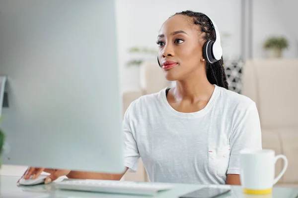 忧心忡忡的年轻黑人妇女在电脑上工作时听音乐的画像 — 图库照片