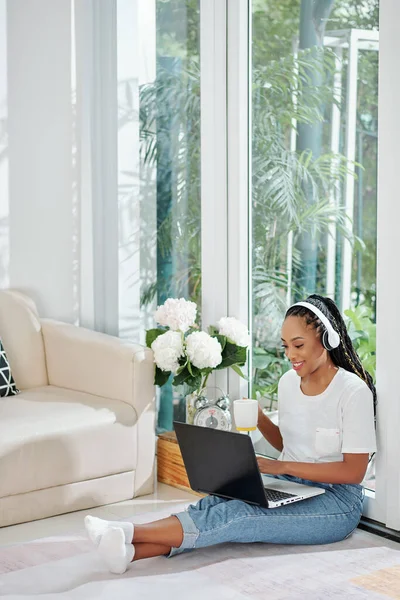 漂亮的黑人妇女 头发蓬乱 坐在公寓的地板上 用笔记本电脑工作 喝咖啡 — 图库照片