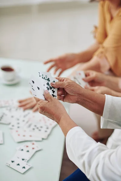 Hands of senior women playing cards and drinking tea when spending weekend together