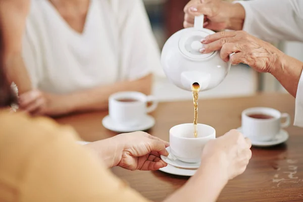 高级妇女的手在宴会上往客人的杯子里倒热茶 — 图库照片