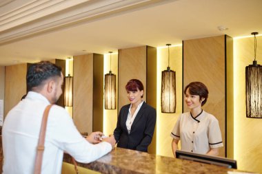 Gülümseyen Asyalı otel resepsiyon yöneticileri misafirlerle konuşuyor ve odayı seçmelerine yardım ediyor.