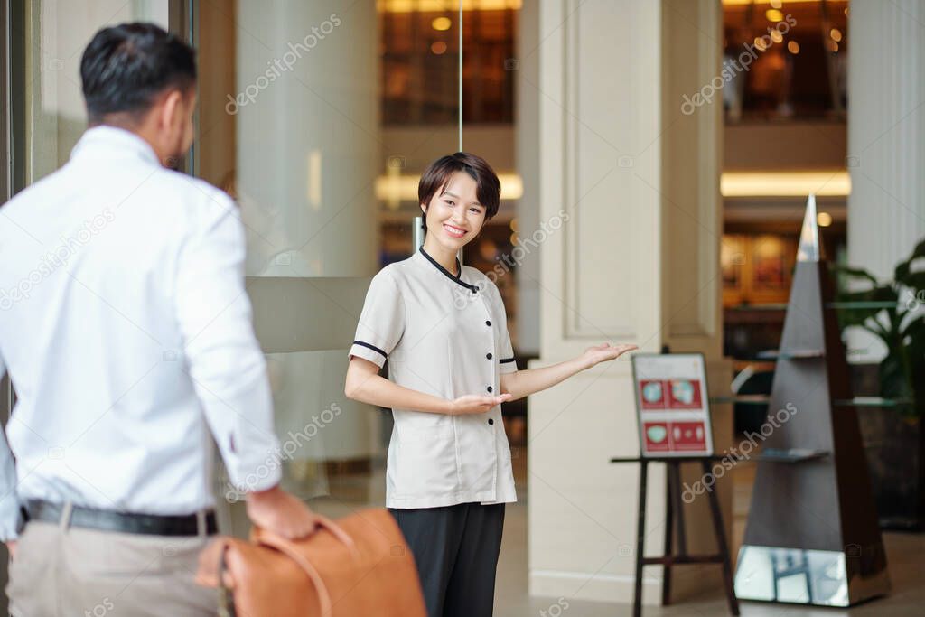 Smiling hospitable concierge welcoming guest at doors of fancy hotel