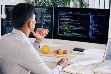 Masasında çalışan ve bilgisayar ekranındaki programlama kodundaki hataları kontrol eden düşünceli yazılım geliştiricisi